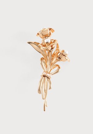 Broche florale ton or avec fleurs sculptées, accents de perles et tige en forme de nœud, présentée sur fond uni.