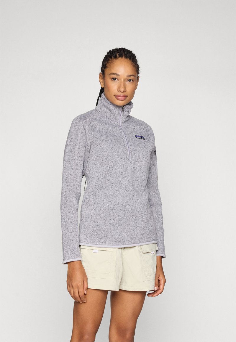 Grijze fleece pullover met hoge kraag en een halve rits aan de voorkant. Bevat een Patagonia-logo op de borst en platte naden. Draagt bij witte korte broek.