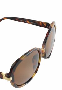 Brūnas bruņurupuča rakšta saulesbrilles ar apaļu dizainu, zelta akcentiem uz kājiņām un pārejojuma lēcām. Izgatavotas no plastmasas, ar spīdīgu virsmu.