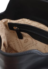 Svart läderhandväska inuti med beige foder som har "Café Noir" logomönster, en zip-ficka och en texturerad tygfinish.