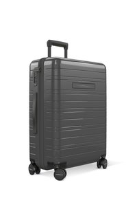Valise rigide de couleur gris foncé mat, avec des rainures verticales, une poignée télescopique et quatre roues pour la mobilité. Équipée d'une fermeture à combinaison.