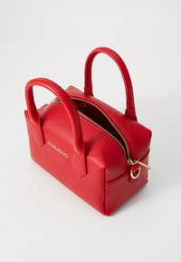 Punane nahast käsipakar, millel on kaks käepidet, tekstureeritud pind, kuldne lukk ja logo ees. Kompaktne ristkülikukujuline kuju.