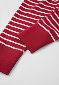 Punainen ja valkoinen raidallinen kangas, joka näyttää lähikuvan hihasta, jossa on ribattuja hihansuita. Tekstuuri on sileä ja joustava.