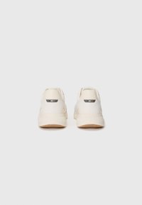 White sneakers with a smooth upper, cream-colored accents, and textured rubber soles. Features a small logo tab on the heel.