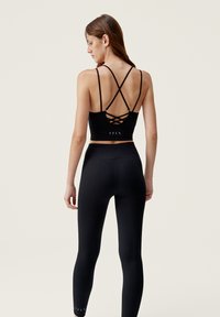 Black cropped tank top with crisscross back straps, paired with high-waisted black leggings featuring textured fabric and discreet accents.