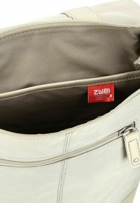Lichtbeige stoffen tas met een gladde textuur. Heeft een rode binnenlabel, ritsluiting en een extra externe ritsvak.