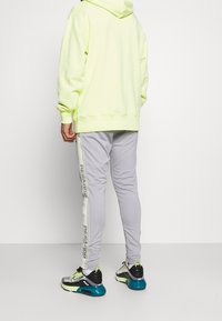 Neon grön huvtröja, grå slim-fit joggers med sidostråk, och svarta och neon sneakers med genomskinlig sula.
