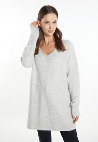 Pulover gri tricotat cu decolteu în V, cu mâneci lungi, manșete și tiv cu nervuri. Textură moale, croială ușor supradimensionată și un model subtil.