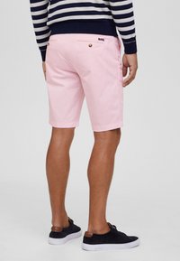 Lichtroze shorts met een gladde textuur, achterzak met knoopdetail, gecombineerd met marineblauwe suède sneakers met bruine accenten.