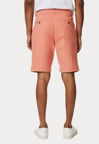 Shorts de couleur corail en coton, dotés d'un devant plat, de passants de ceinture et de deux poches arrière avec fermetures à bouton. Finitions à hauteur du genou.