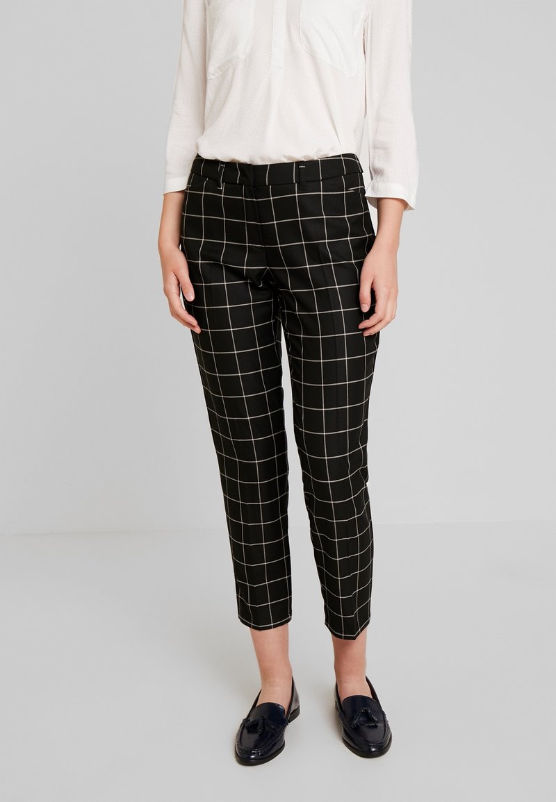 Czarne spodnie w kratę z wzorem siatki, skrócony fason, gładki materiał oraz średni stan, w połączeniu z ciemnymi loafersami i białą koszulą.