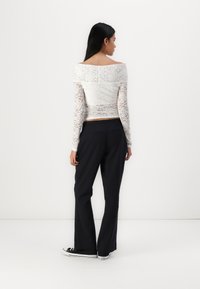 Top blanc en dentelle à épaules dénudées avec des manches longues, associé à un pantalon noir évasé et des baskets noires. Texture lisse avec un motif floral en dentelle.