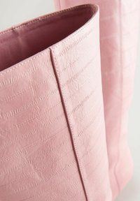 Bolso tote de cuero texturizado en color rosa con surcos verticales, que presenta un interior liso y bordes cosidos.
