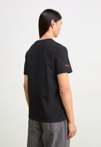 Black short-sleeve t-shirt made of cotton, featuring a red Puma logo on the left sleeve and a classic crew neck design.