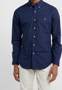 Mörkblå knapp-up-skjorta i bomull, med klassisk krage, långa ärmar och liten logotyp på bröstet. Slät textur.