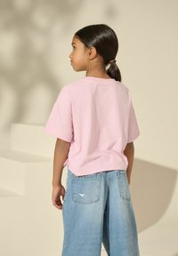 Camiseta de algodón rosa de manga corta y corte relajado, combinada con jeans de mezclilla de pierna ancha en azul claro que presentan un detalle desgastado en el bolsillo trasero.