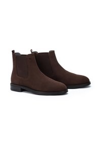 Bottines Chelsea en daim marron avec panneaux élastiques sur les côtés, languettes de tirage et semelle en caoutchouc plate. Texture lisse avec un design classique.