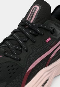 Czarne buty sportowe z teksturowaną cholewką, różowymi akcentami i szarymi sznurówkami. Posiadają amortyzującą podeszwę środkową oraz wzorzyste nałożenia po bokach.