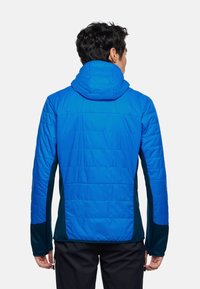 Veste bleue rembourrée avec une capuche, présentant une texture matelassée et des panneaux latéraux vert foncé. Le design comprend des manches longues et un dos ajusté.