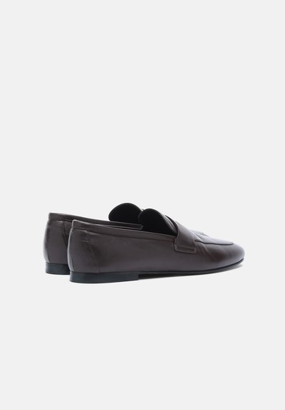 Paire de mocassins en cuir marron foncé sans lacets avec de petits talons noirs, vue de profil sur fond blanc uni.