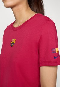 Rød bomull T-skjorte med Barcelona-logo på brystet og stripedesign på ermene med en blå Nike swoosh.