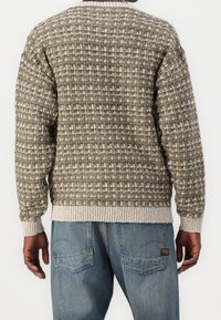 Stickad tröja i grönt och vitt med ett strukturerat mönster. Har ribbstickade muddar och fåll, samt en rund halsringning. Matchas med blå jeans.