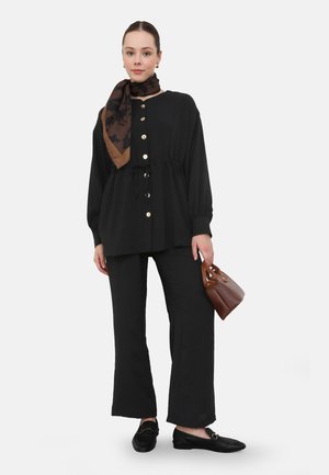 Black long-sleeve button-up top with a drawstring waist, paired with black wide-leg pants. Accessories include a patterned brown scarf and small brown handbag.