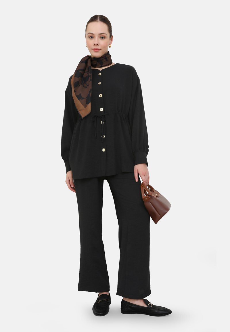 Black long-sleeve button-up top with a drawstring waist, paired with black wide-leg pants. Accessories include a patterned brown scarf and small brown handbag.