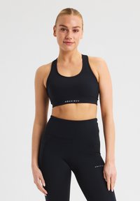 Conjunto de sujetador deportivo y leggings negros, confeccionado con una tela suave y elástica. El sujetador tiene un escote redondeado y el logotipo de la marca en la parte inferior.