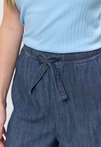 Top albastru cu model nervurat, asortat cu pantaloni din denim închis, prevăzuți cu talie elastică și o fundă din material. Denimul are o textură moale, cu variații subtile.
