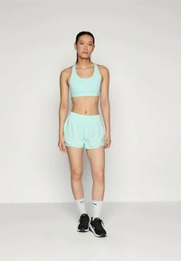 Lys teal idretts-bh og matchende shorts; lett og pustende materiale; kombinert med svarte joggesko og hvite sokker.