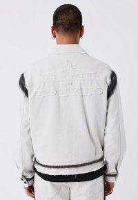 Witte denimjack met zwarte accenten, met een versleten ontwerp, geborduurd logo en rafelige zoom. Lange mouwen en voorzakken.