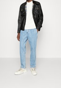 Černá kožená bunda se dvěma kapsami na prsou, bílé tričko, světle modré džíny a béžové tenisky se šedými akcenty. Neformální outfit.