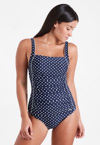 Maillot de bain une pièce bleu marine à pois, avec décolleté carré, bretelles larges, détails froncés et accents blancs. Texture lisse, design ajusté.
