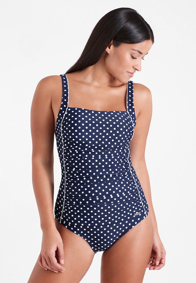 Maillot de bain une pièce bleu marine à pois, avec décolleté carré, bretelles larges, détails froncés et accents blancs. Texture lisse, design ajusté.