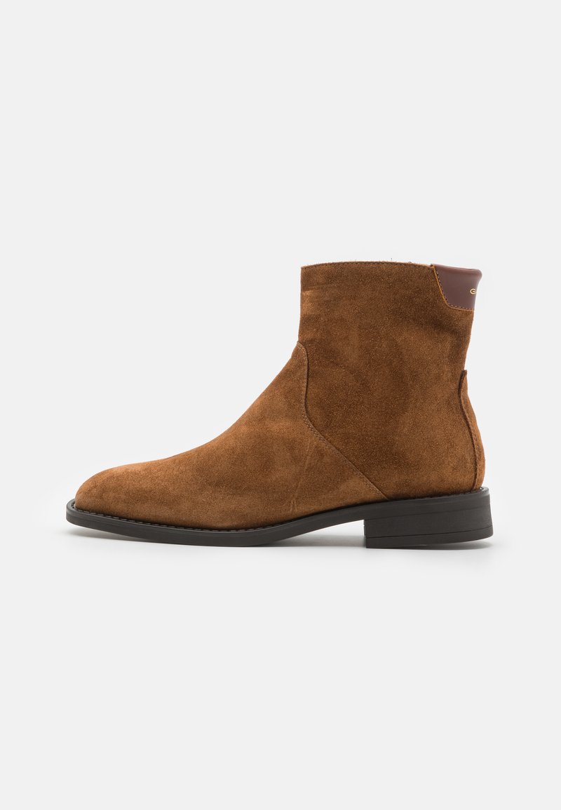 Schwarze Wildleder-Ankle-Boots mit leicht spitz zulaufender Zehenpartie, flachem schwarzen Absatz und einem kleinen braunen Akzent an der Rückseite. Glatte Textur und minimalistisches Design.