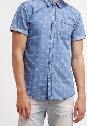 Camisa de mezclilla de manga corta en azul claro con un patrón de palmeras blancas, diseño de botones y un bolsillo en el pecho. Puños de manga enrollados.