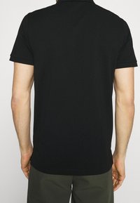 Svart pikétröja med korta ärmar, subtil krage och rak skärning. Slät textur, inga mönster eller synliga hårdvarudetaljer.