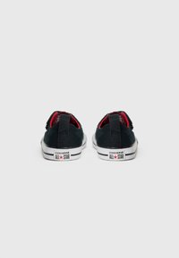 Melnas audekla kedas ar sarkaniem akcentiem, ar zemu augumu, baltu gumijas zoli un Converse All Star zīmolu uz papēža.