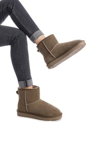 Botines de ante marrón con un forro suave, punta redonda y suela de goma texturizada. Presentan una costura cosida y una lengüeta trasera.