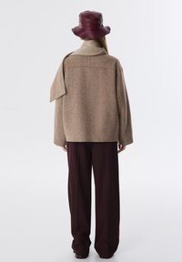 Bruine herringbone oversized jacket met brede mouwen en een schouderflap. Gecombineerd met donker bordeaux brede broekspijpen en een bijpassende bucket hat.