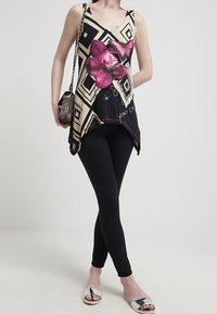 Black and cream geometric-patterned tank top with a pink orchid print, paired with black leggings and metallic-accented sandals.