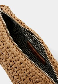 Torbka z plecionego słomy z srebrnym suwakiem, wewnątrz z czarnym wzorzystym podszewką i brązową skórzaną etykietą. Teksturowane wykończenie zewnętrzne.