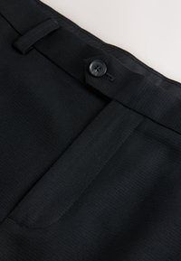 Vita di pantaloni neri con chiusura a bottone, tessuto strutturato, design frontale piatto e passanti per cintura. Bordi cuciti con cura e linee pulite.