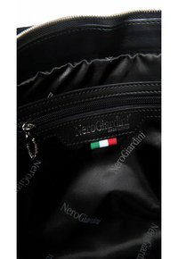 Interno nero di una borsa con una tasca con zip, un'etichetta in pelle impressa con "NeroGiardini" e un piccolo accento della bandiera italiana. Texture liscia.