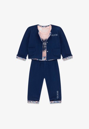 Navy trenirka z jakno na gumb z dvema žepoma in cvetličnimi manšeti, v kombinaciji s usklajenimi hlačami. Roza majica z grafiko srca v notranjosti.