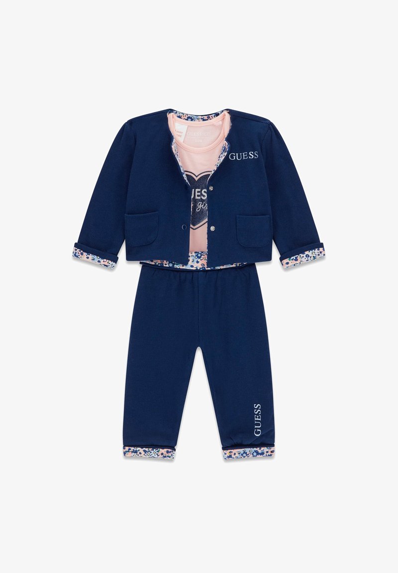 Marineblauer Trainingsanzug mit einer Knopfleistenjacke, die zwei Taschen und Blumenmanschetten hat, kombiniert mit passenden Hosen. Rosa Shirt mit Herzgrafik innen.