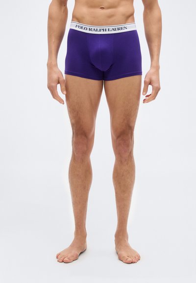 Άνδρας που φοράει μωβ boxer Ralph Lauren, όρθιος ξυπόλυτος πάνω σε απλό λευκό φόντο.