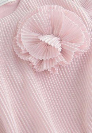 Rožnata plisirana tkanina ima plastni volanček, z teksturirano površino in subtilnim leskom. Oblikovanje poudarja mehkobo in dimenzijo.