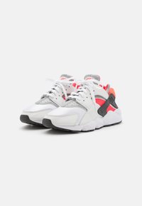 Białe i szare sneakersy z różowymi akcentami, wykonane z połączenia skóry i siateczki, z wiązaniami i teksturowaną gumową podeszwą.